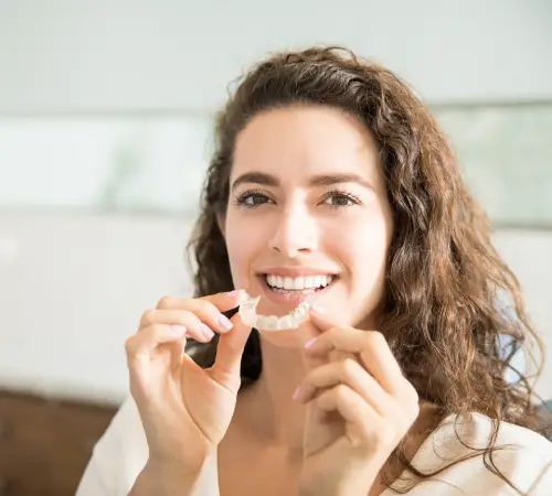 Smiling woman with curly hair holding a clear aligner